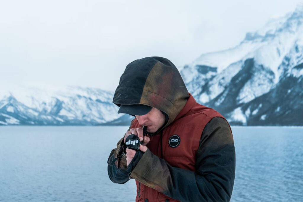 A man with a hood on using a dab rig, with a winter-themed scenery in the background.