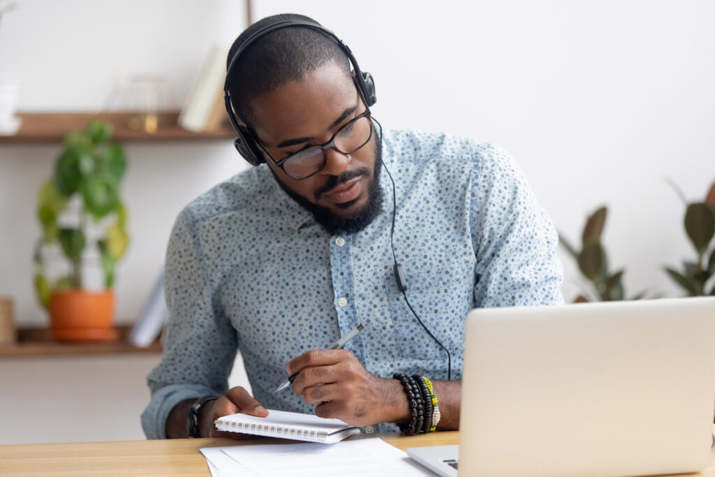 Focused african businessman in headphones writing notes watching webinar