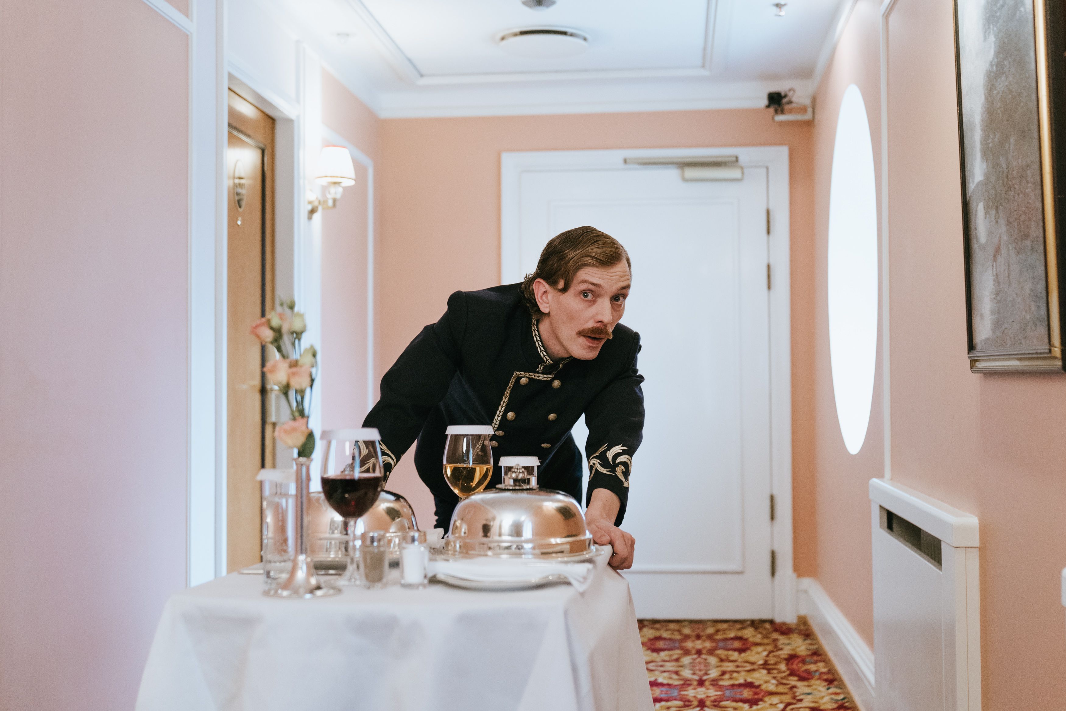 Hotel staff member quietly delivers room service through a luxury hotel corridor, illustrating discreet hospitality.